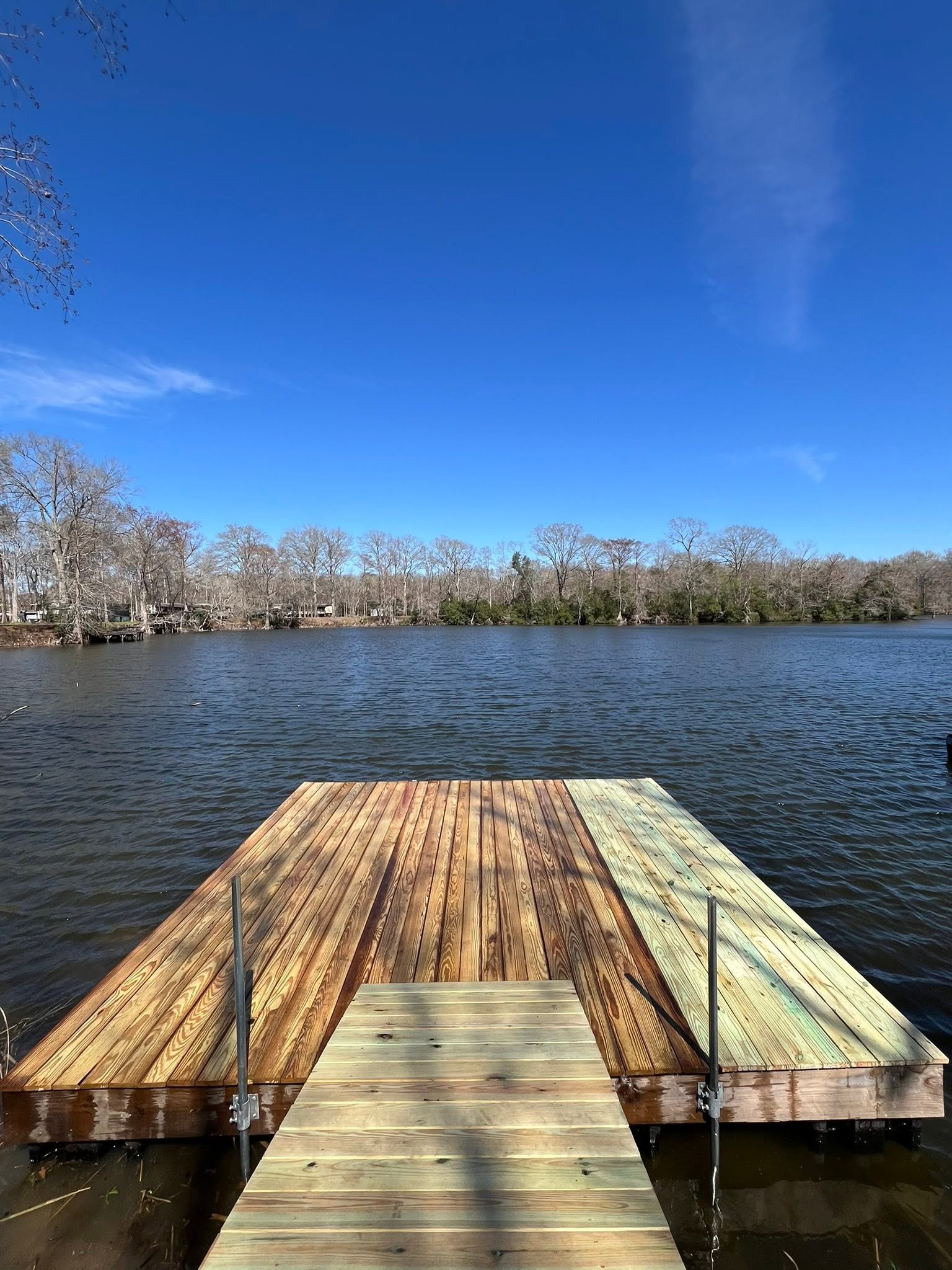 View down a timber dock toward open water and a blue Louisiana sky
